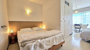 Ein Hotelzimmer mit einem großen Bett, zwei Nachttischlampen, einem hölzernen Kopfteil und Blick durch ein Fenster nach draußen.
