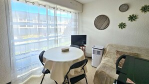Ein kompakter Wohnbereich mit Esstisch, Sofa, Fernseher und einer kleinen Klimaanlage.