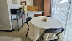 Eine kleine Küche mit Mikrowelle, Herd und Kühlschrank. Ein Esstisch mit Stühlen und eine kleine Schranke sind ebenfalls vorhanden.