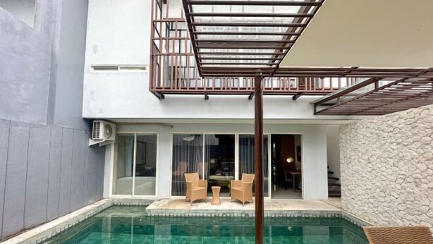Une piscine agrémentée d’une pergola, d’un espace salon extérieur et d’un mur en pierre.