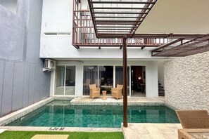 Une piscine agrémentée d’une pergola, d’un espace salon extérieur et d’un mur en pierre.