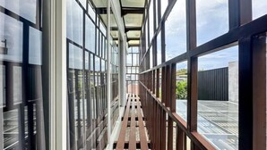 Une passerelle couverte, dotée de rampes en verre et d’un plancher en bois, mène à un espace sur le toit d’où l’on peut admirer le ciel et les bâtiments environnants.