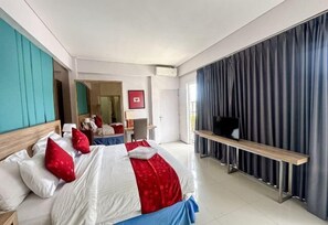 Ein Hotelzimmer mit Bett, Fernseher auf einem Schrank, Schreibtisch mit Stuhl und einem großen Fenster mit Vorhängen.