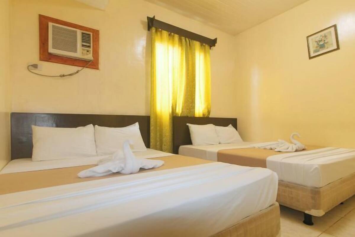 Une chambre d’hôtel avec deux lits, un climatiseur fixé au mur, un rideau et un tableau encadré.