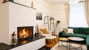 A living room with a fireplace, a green sofa, a white armchair, and a small round table. - Ruhestein - Quartier characterful flat,  122m², near the railway station & Iven (Baiersbronn)