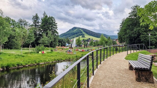 A riverside walkway with benches, a small bridge, and a picnic area with tables and chairs. - Ruhestein - Quartier characterful flat,  122m², near the railway station & Iven (Baiersbronn)