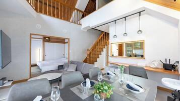 A modern hotel room with a dining area, a staircase, and a view of the kitchen.