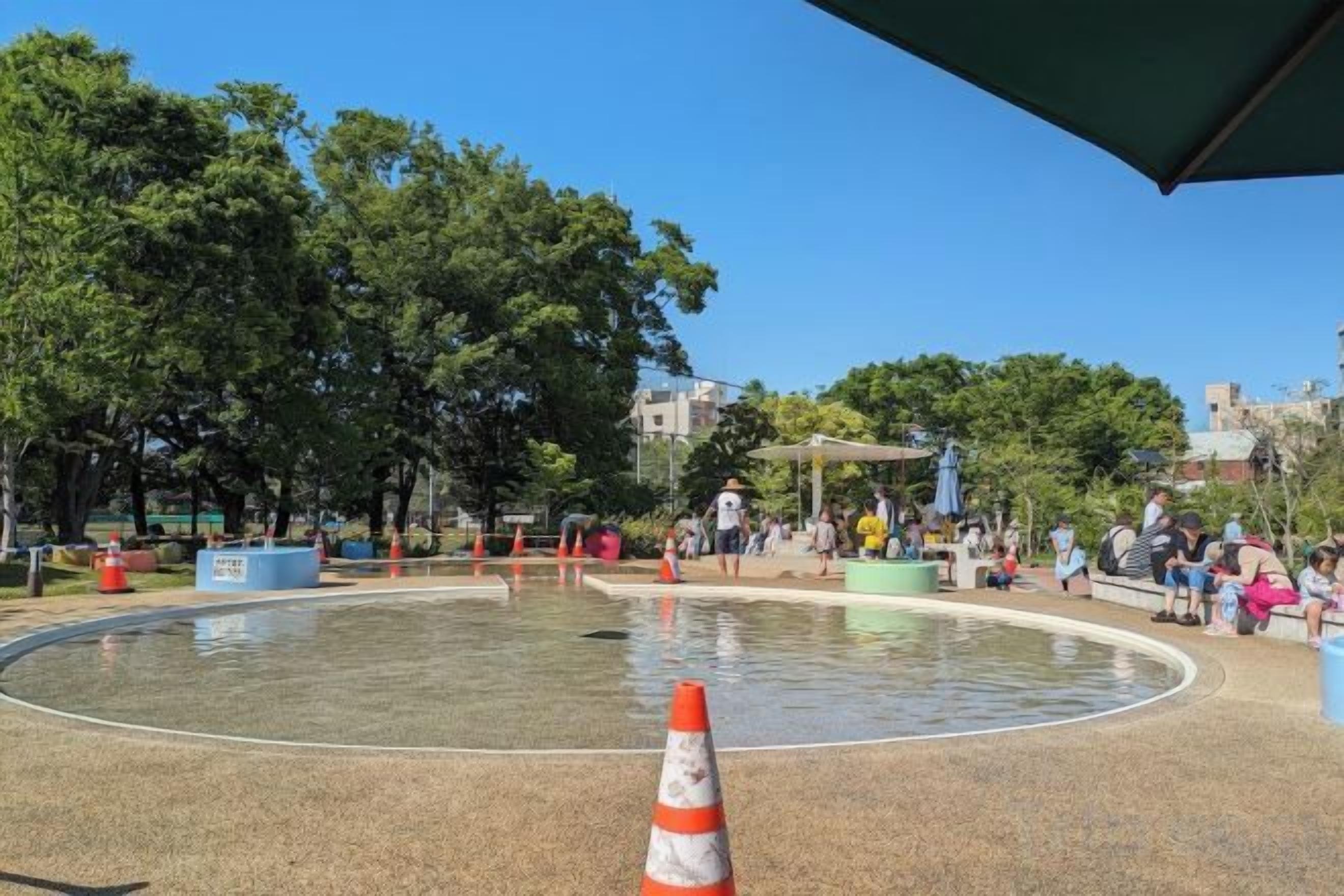 Ein Außenbereich mit einem kreisförmigen Wasserspiel, Sitzgelegenheiten und Bäumen.