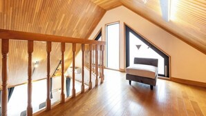 Amplia habitación en el ático con escalera de madera, un ventanal grande y un sofá moderno.