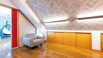 A spacious room with a herringbone-patterned ceiling, wooden flooring, a grey armchair, and a red curtain.