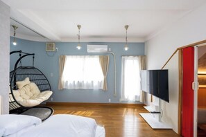 Une pièce avec un lit, un fauteuil suspendu, une télévision et une porte rouge.
