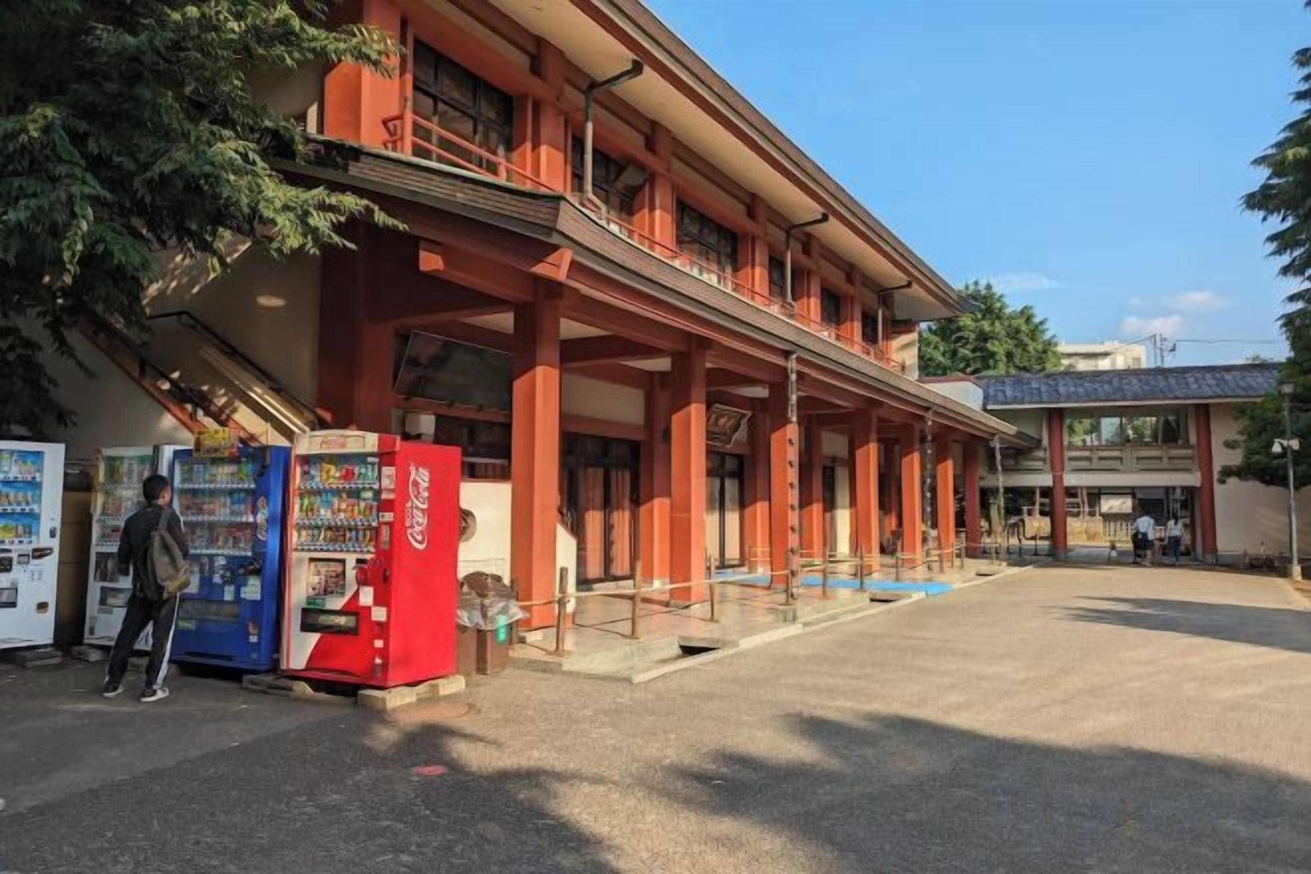 A building with a red facade and a covered entrance. There are vending machines on the sidewalk.