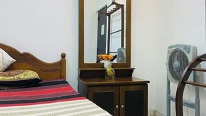 A bedroom with a bed, a dresser, a mirror, a fan, and a door. - Suriya Haven Homestay (Badulla)