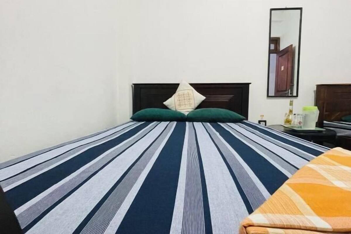 Un lit simple avec une couvre-lit à rayures, un oreiller vert et une tête de lit en bois.