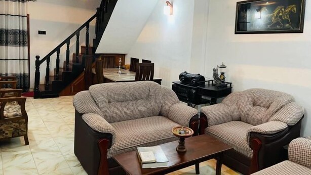 A living room with two patterned sofas, a wooden coffee table, and a staircase leading to an upper floor. - Suriya Haven Homestay (Badulla)