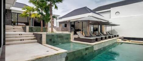 A modern pool area with clear water, lounge chairs, and a covered seating area.