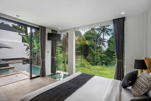A modern bedroom with a large bed, a TV, and a view of a lush garden. - Villa Green Paradise by BaliSuperHost (Bali)