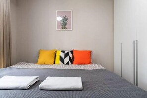 A neatly made bed with a gray bedspread and three pillows in yellow, black, and orange.
