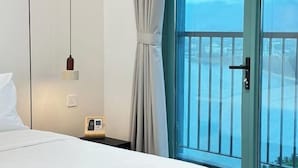 Een hotelkamer met een bed, een nachtkastje met een telefoon, een hanglamp en uitzicht door een glazen deur.