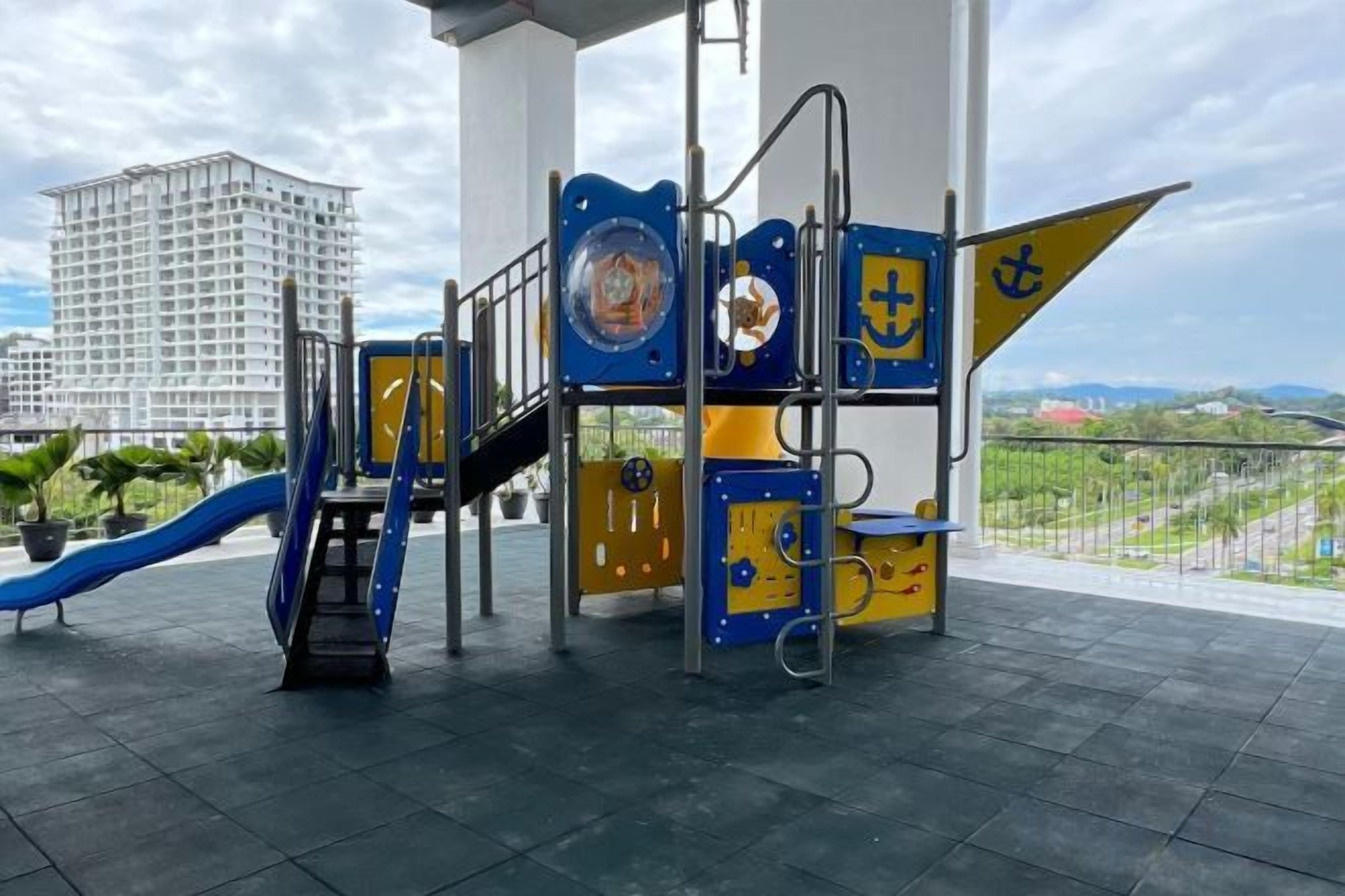 Um parquinho com escorregador e estruturas de escalada, com a paisagem urbana e um céu claro ao fundo.