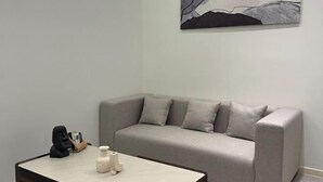 Een moderne woonkamer met een grijze bank, een klein bijzettafeltje en een minimalistisch schilderij aan de muur.