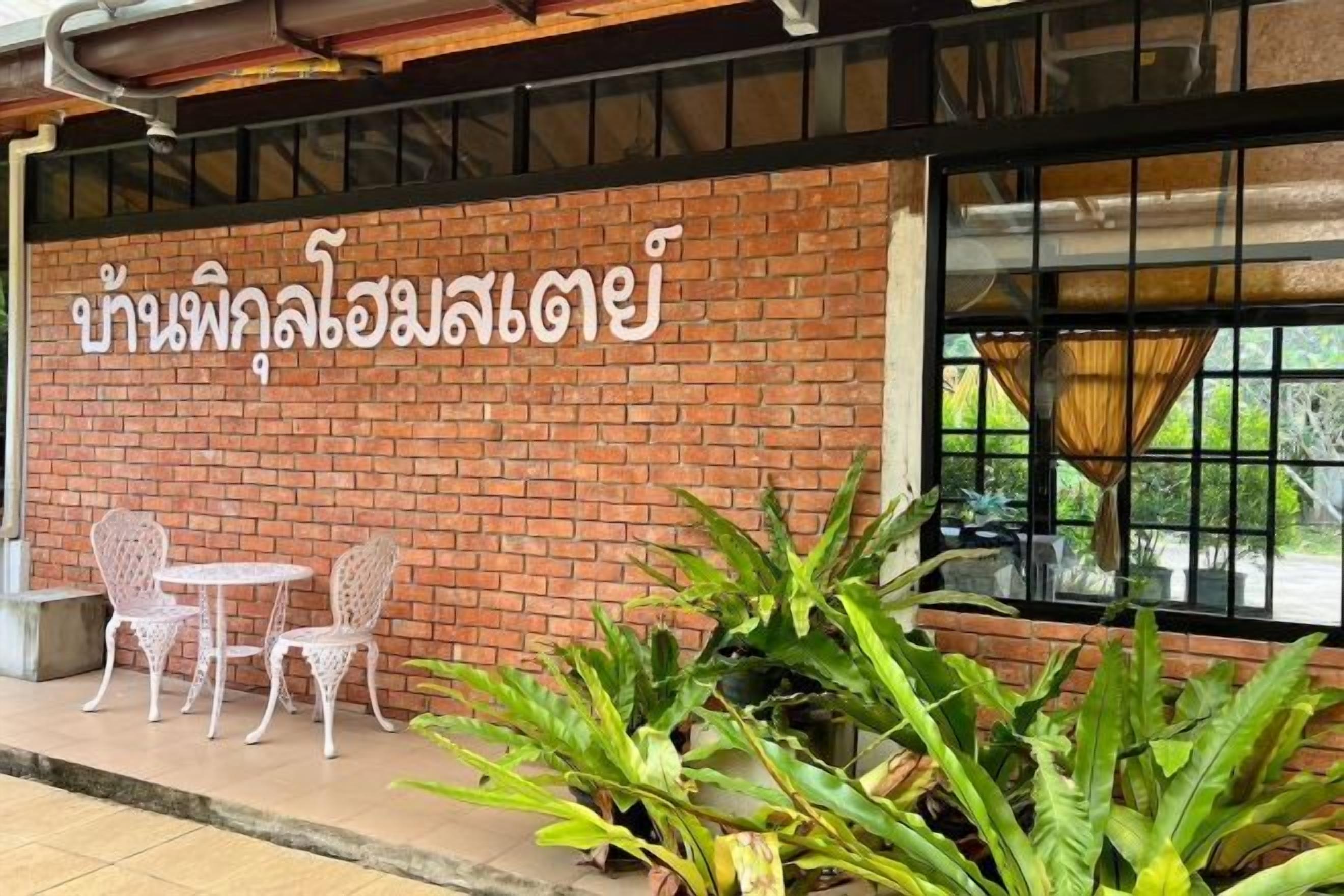 A brick wall with Thai script, two white chairs, and potted plants.