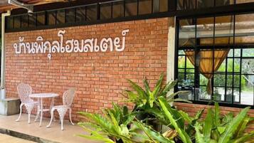 A brick wall with Thai script, two white chairs, and potted plants.