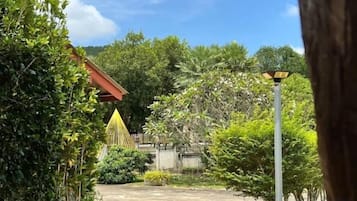 A garden with a pathway leading to a building with a red roof, surrounded by greenery and a clear sky.