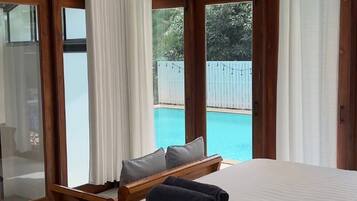 A bedroom with a large window, a bed, a wooden headboard, and a view of a swimming pool.