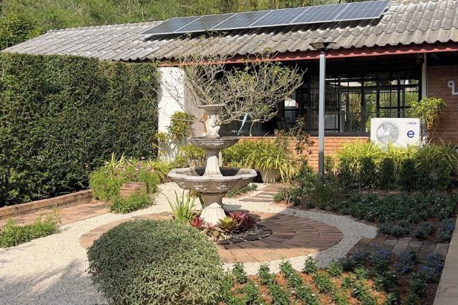 A garden with a central fountain, a solar panel roof, and a brick building with a window and an air conditioning unit.