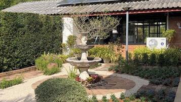 A garden with a central fountain, a solar panel roof, and a brick building with a window and an air conditioning unit.