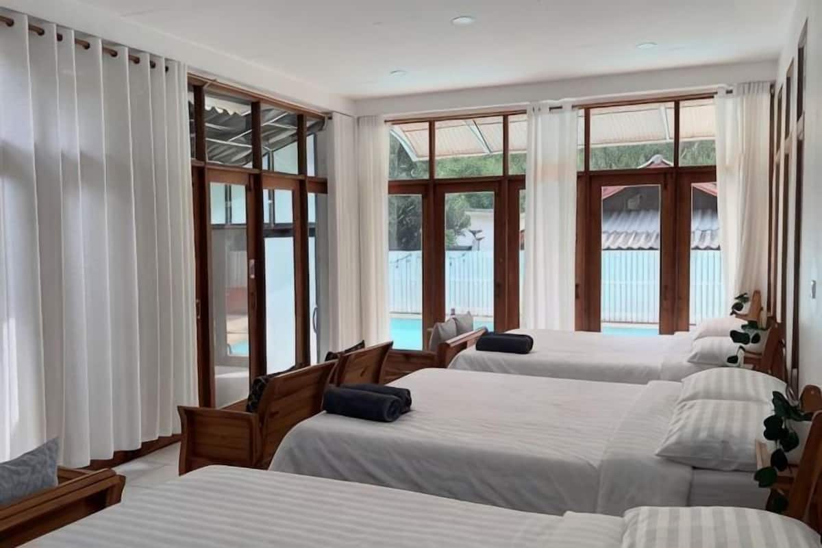 A hotel room with three beds, large windows, and a view of the outside.