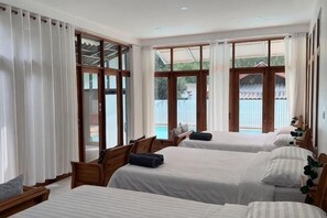 Une chambre d’hôtel avec trois lits, de grandes fenêtres et une vue sur l’extérieur.