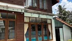 A wooden building with large windows, a pool, and a covered patio area. - Pikul Homestay (Hat Yai)