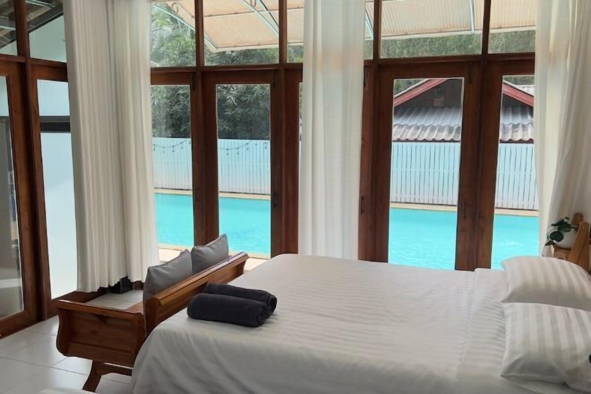 Une chambre avec un grand lit, un banc en bois et une vue sur une piscine.