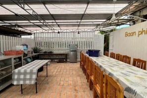 Un espace extérieur abrité, aménagé pour les repas, avec une longue table, des chaises et un réfrigérateur.