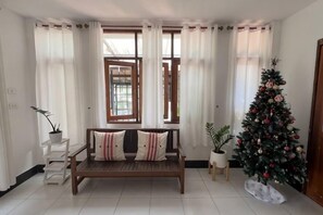 A room with a wooden bench, a Christmas tree, and a window with curtains. - Pikul Homestay (Hat Yai)