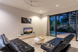 A modern living room with a flat-screen TV, leather sofas, a white ottoman, and a ceiling fan. - Modern 3 Bedroom Boutique Pool Villa (Phuket)