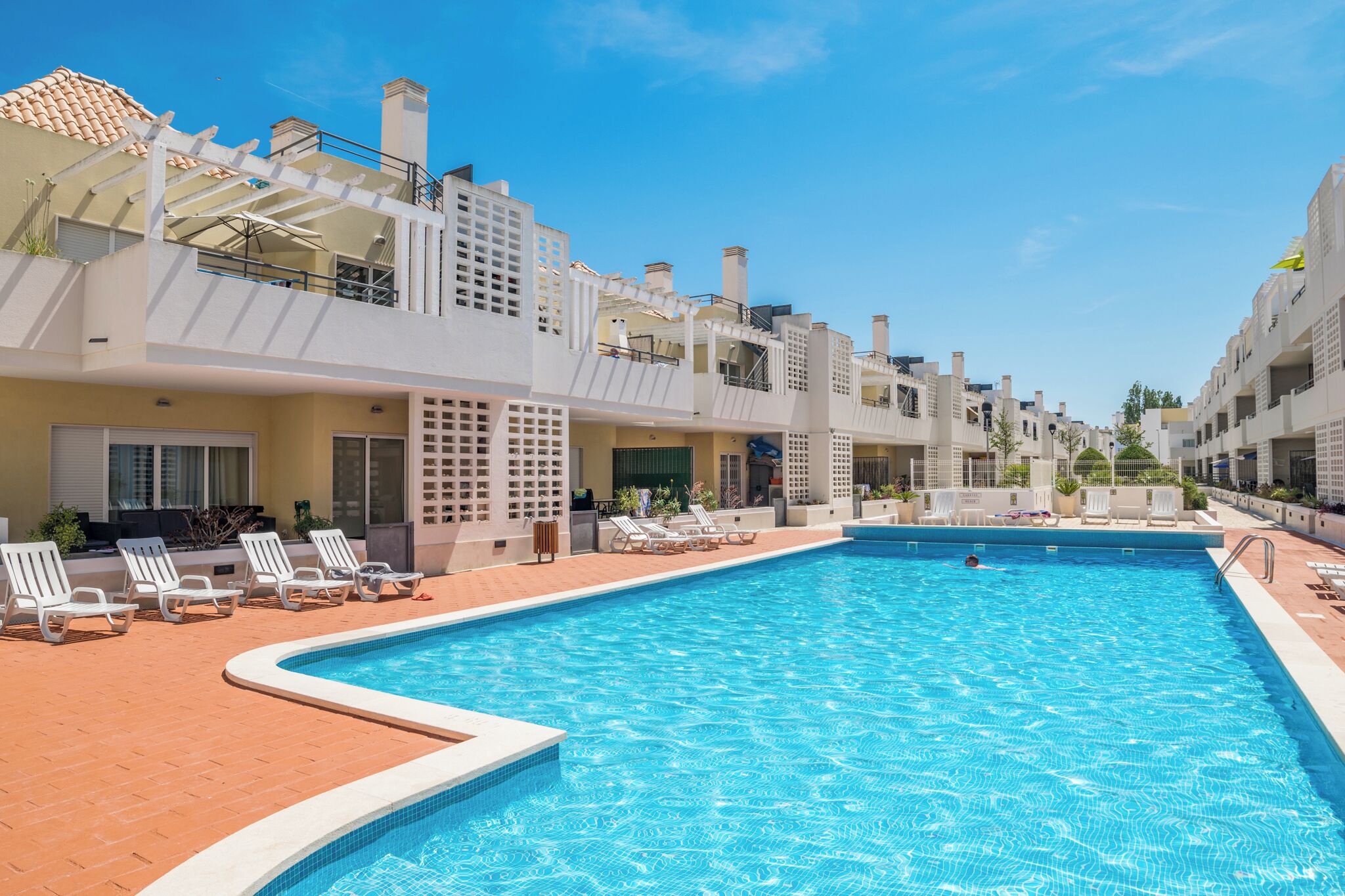 A swimming pool with lounge chairs and a clear blue sky.