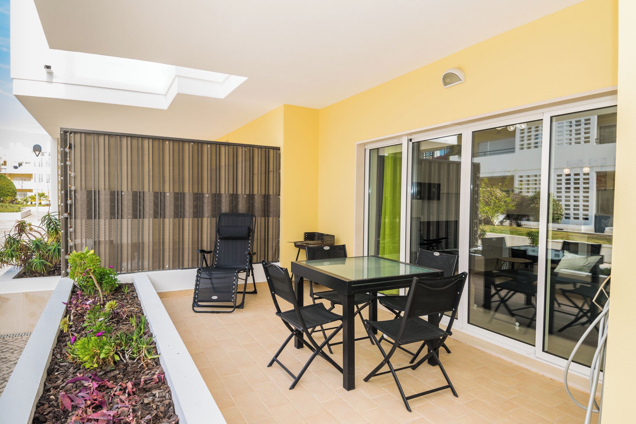 A patio area with a glass table and chairs, a small table with a chair, and a vertical garden.
