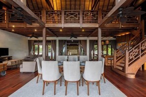 A spacious living area with a wooden ceiling, a dining table with chairs, a sofa, and a TV. - Khaya Luxury Villas (Bali)