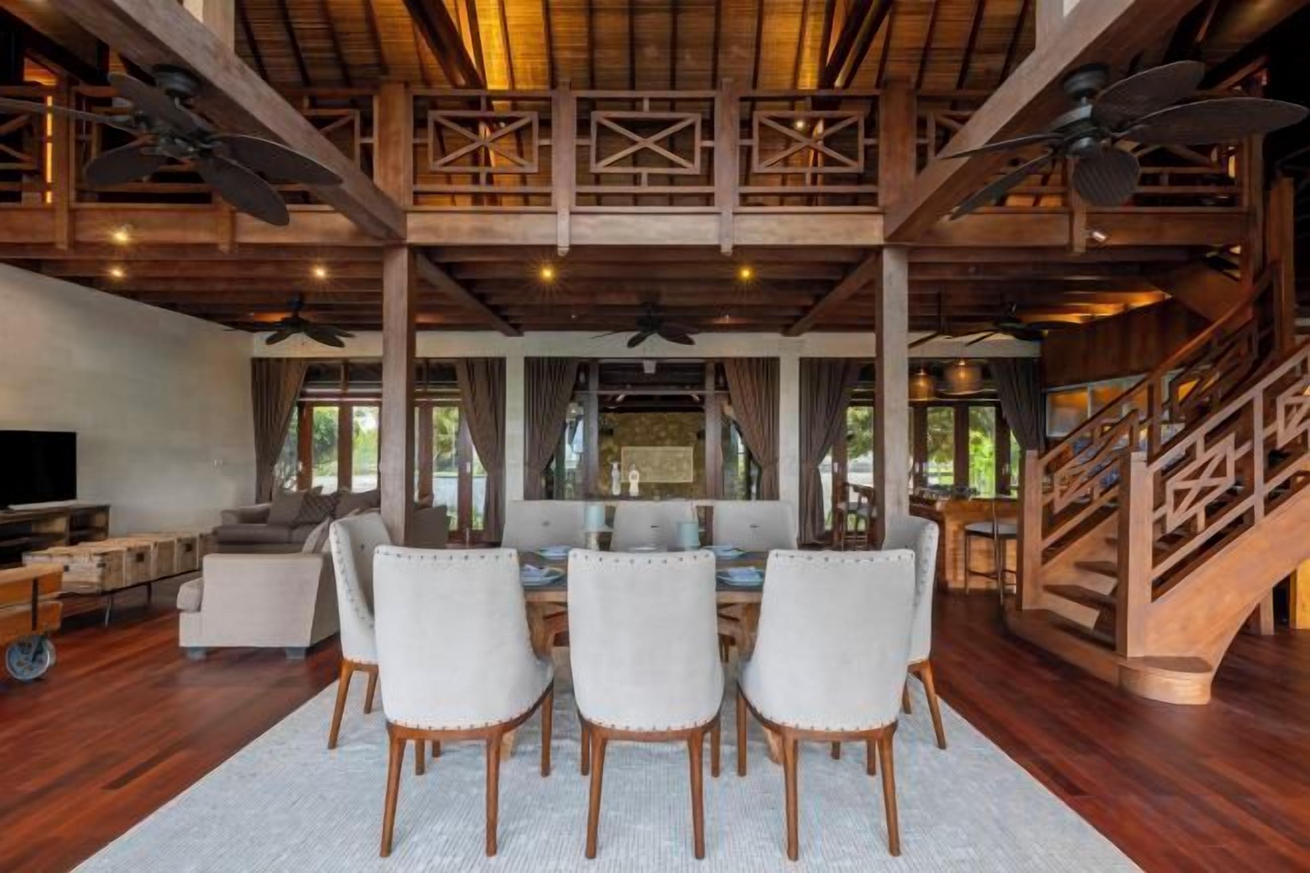 A spacious living area with a high ceiling, wooden beams, a dining table with chairs, a sofa, and a TV.