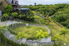 A landscaped garden with a circular lawn, palm trees, and a stone staircase leading to a building. - Khaya Luxury Villas (Bali)