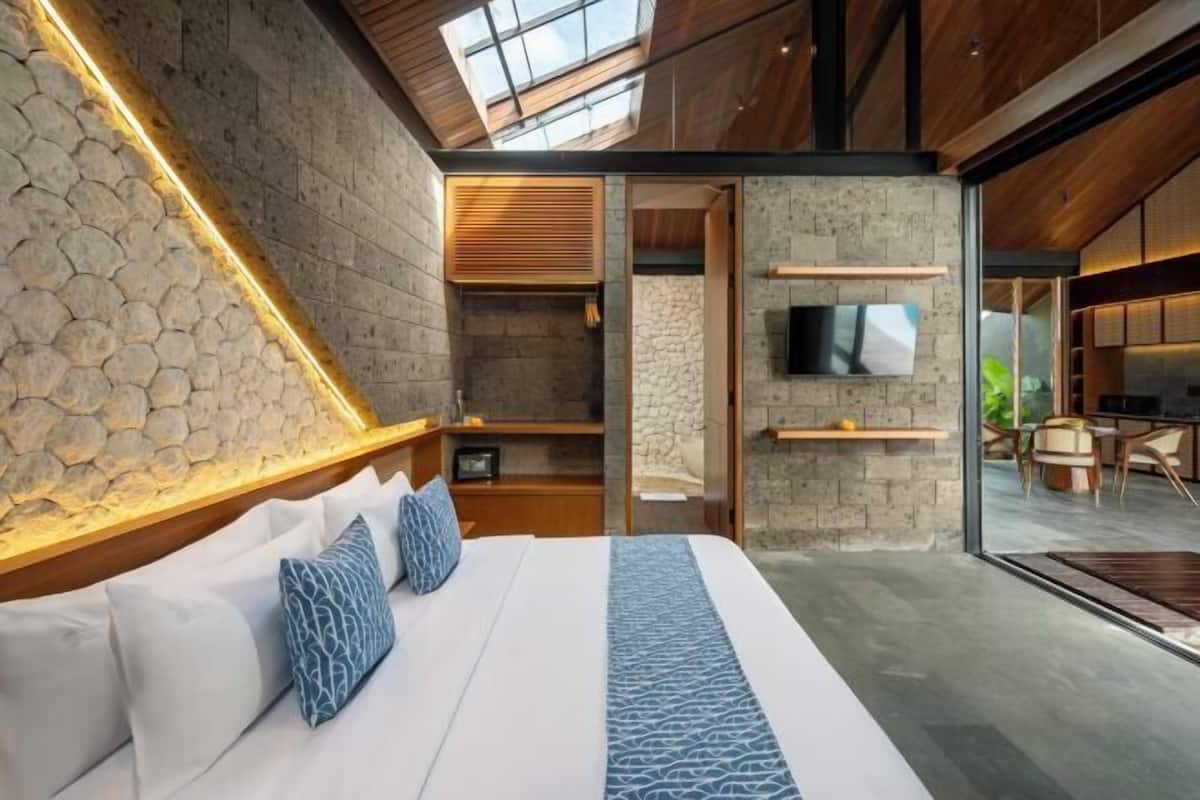 A modern bedroom with a stone accent wall, a large bed, a TV, and a glass door leading to a balcony.