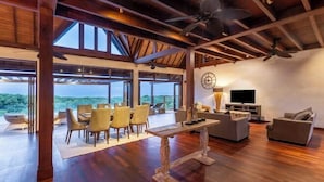 A spacious living area with a dining table, sofas, and a TV. Large windows offer a view of the outdoors. - Khaya Luxury Villas (Bali)