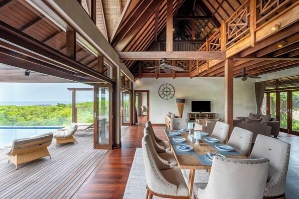 A spacious dining area with a long table, multiple chairs, and a television. - Khaya Luxury Villas (Bali)