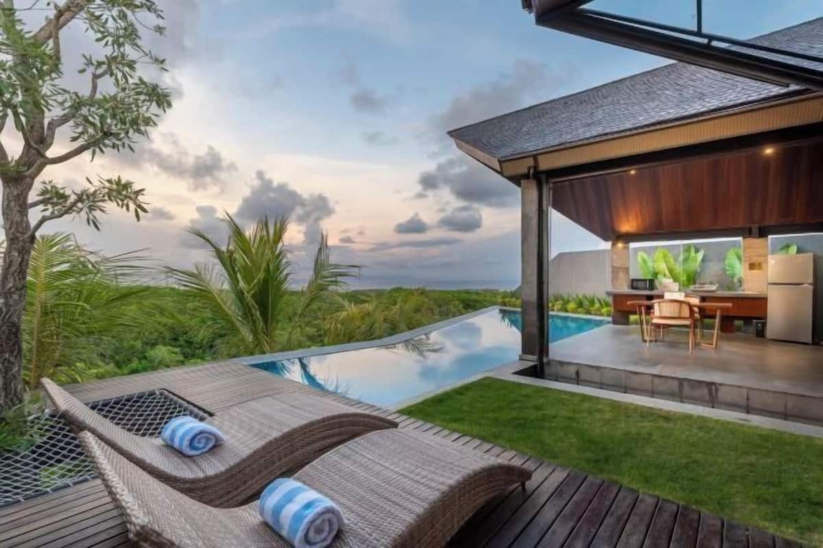 A modern outdoor pool area with lounge chairs, a dining area, and a view of the surrounding landscape.