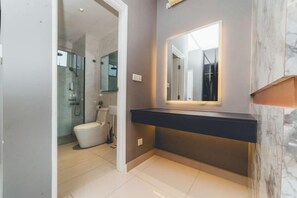 A modern bathroom with a glass shower enclosure, a white toilet, and a dark countertop with a mirror. - Twin Galaxy Residences (Johor Bahru)