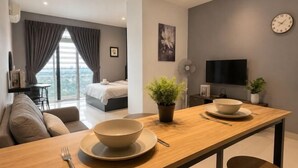 A modern hotel room with a wooden dining table, a bed with a view, a TV, and a potted plant. - Twin Galaxy Residences (Johor Bahru)