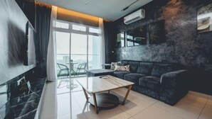 A modern living room with a dark-colored sofa, a glass coffee table, and a large window offering a view of the city. - Twin Galaxy Residences (Johor Bahru)